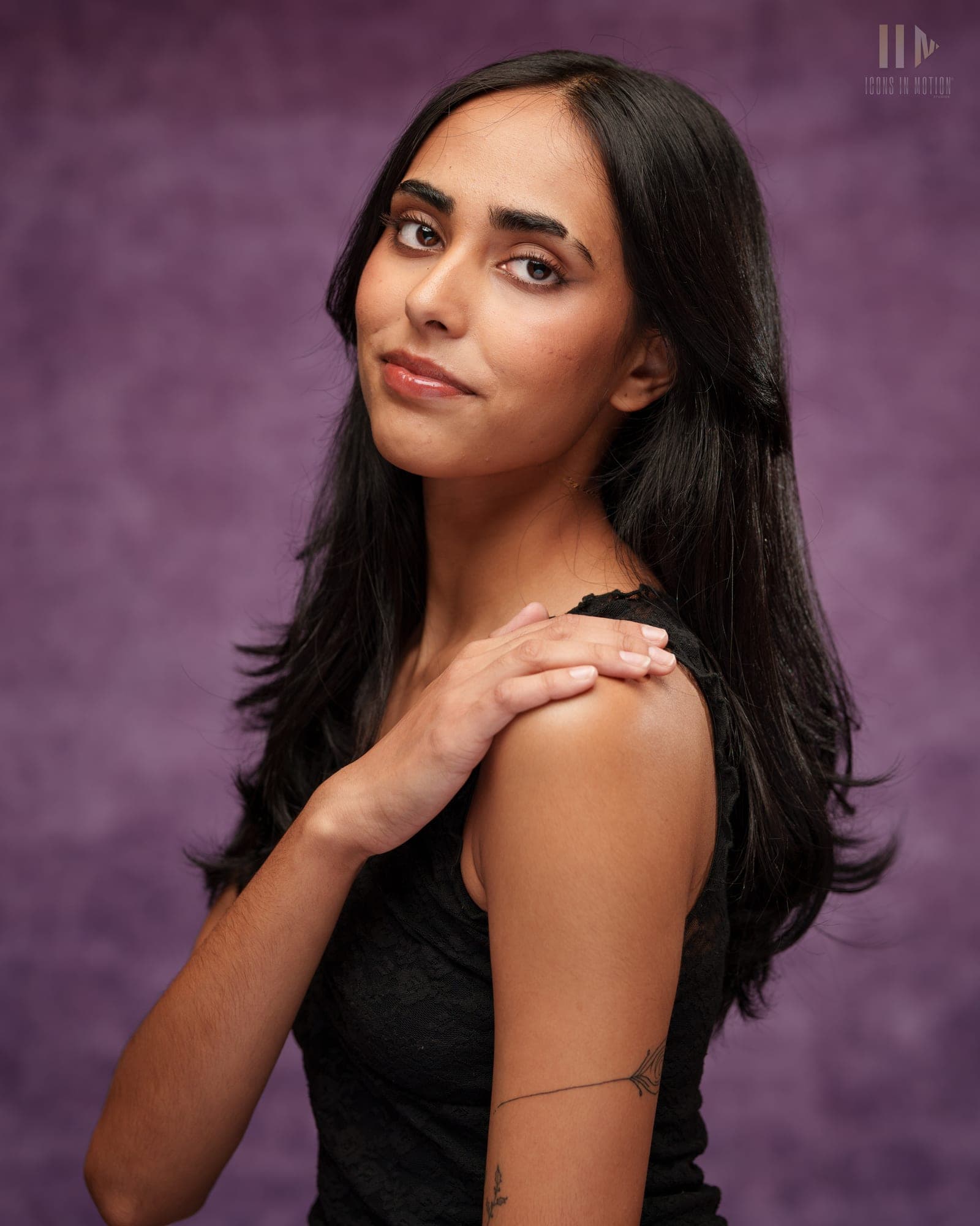 Studio portrait of a person with long dark hair turning to look over one shoulder