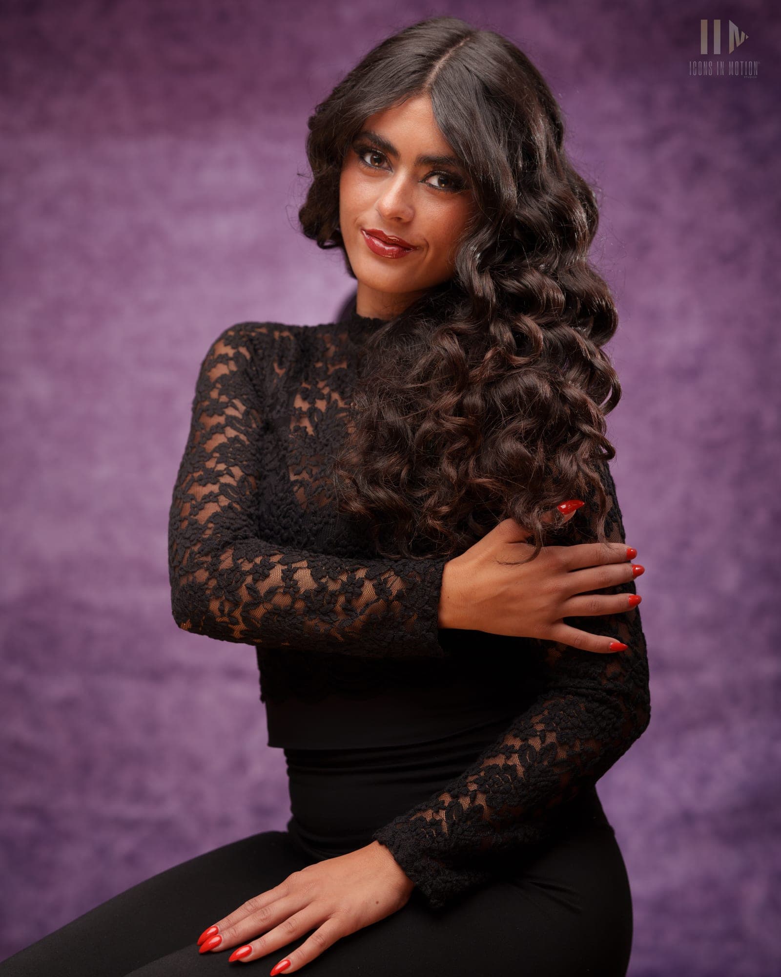 Seated studio portrait of a person in a black lace top with arms crossed