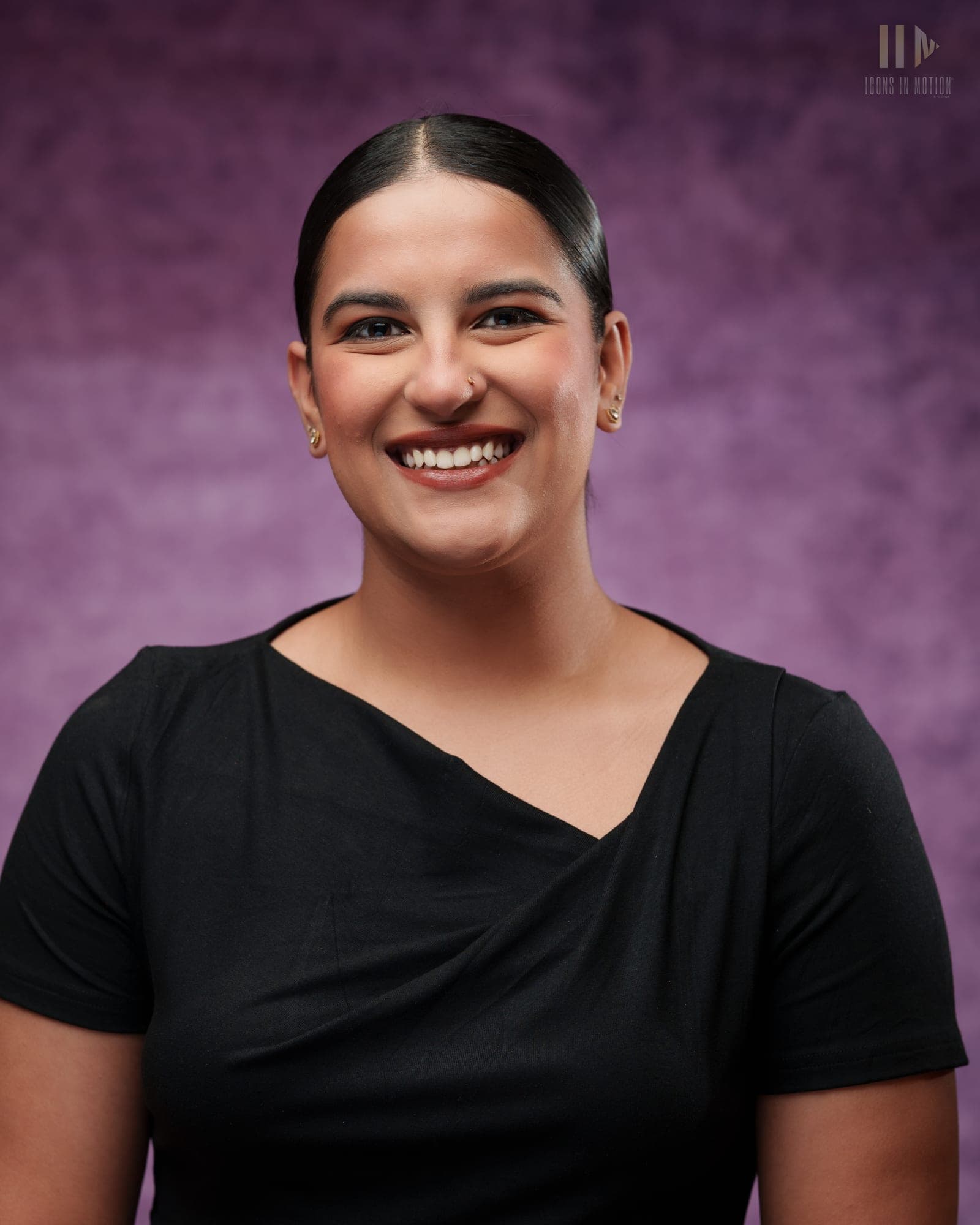 Studio headshot of a person laughing, hair tied back, in a black top