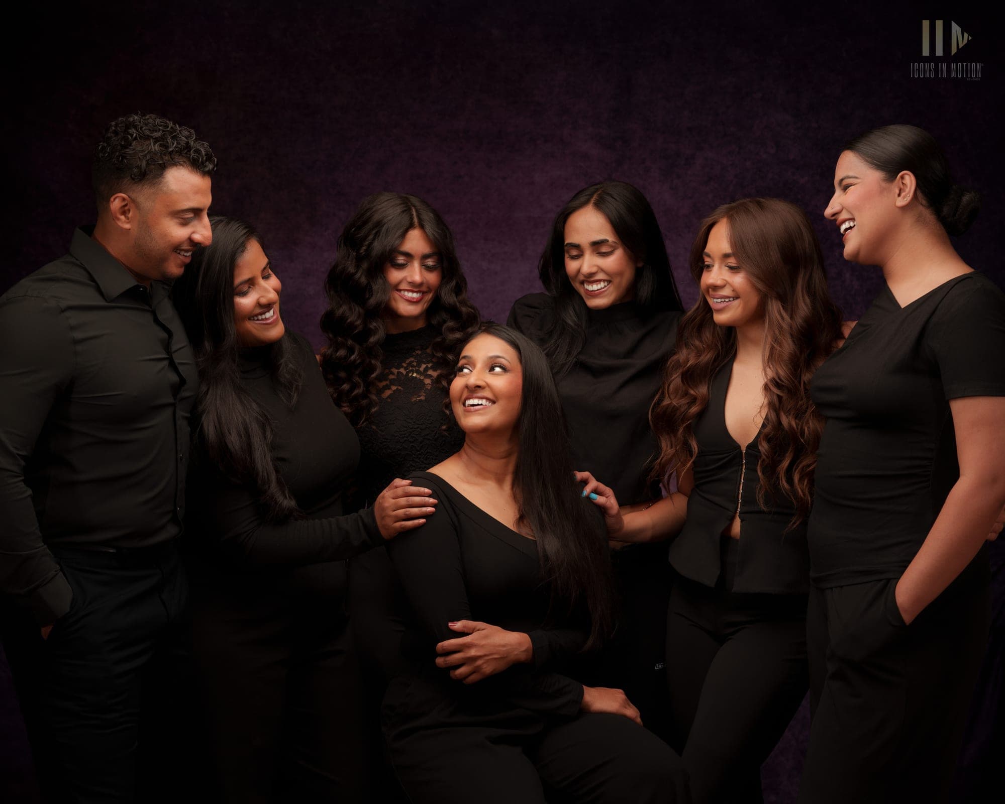 Group studio portrait of seven people in black outfits laughing together