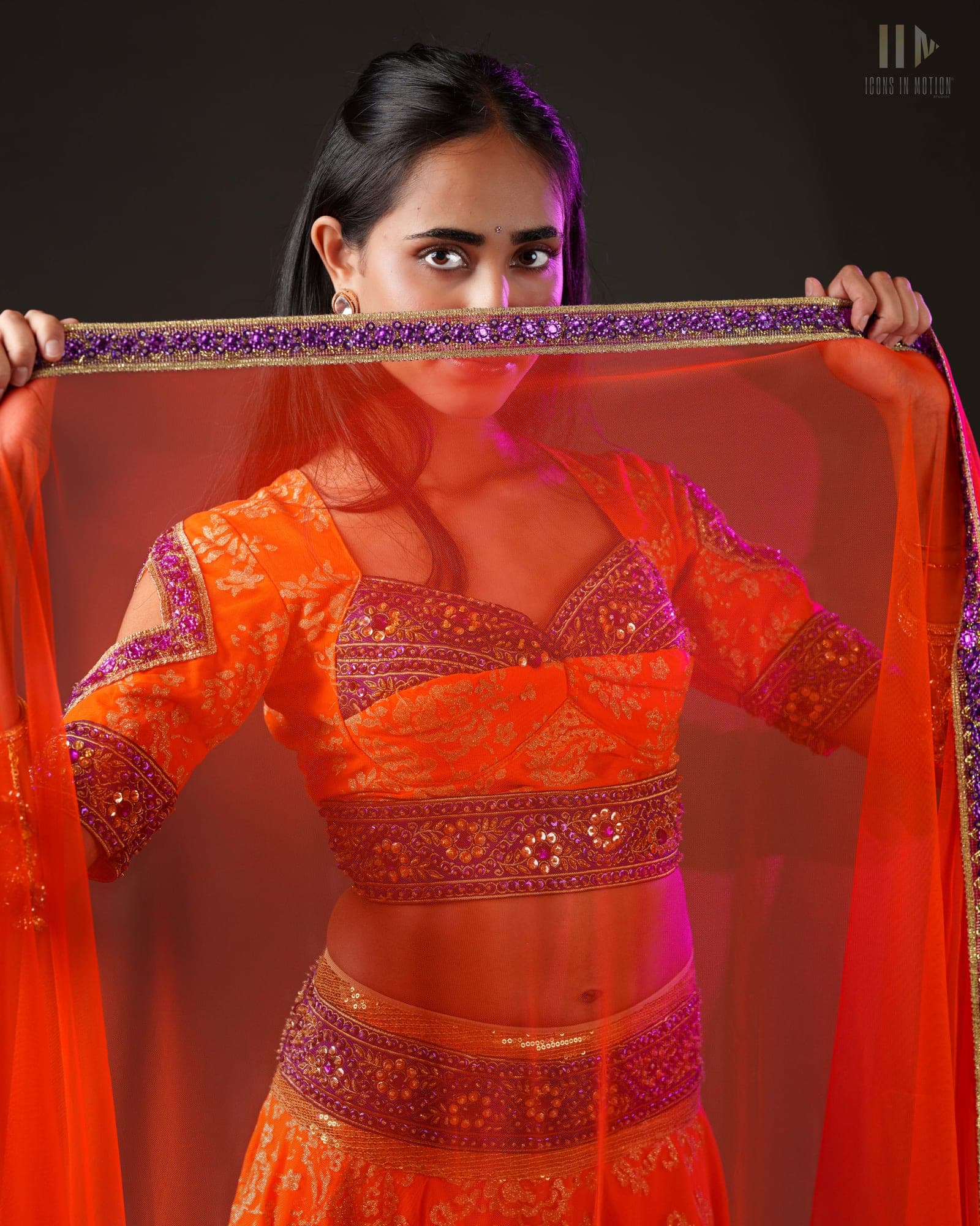 Dancer in an orange embroidered lehenga holding a dupatta stretched overhead