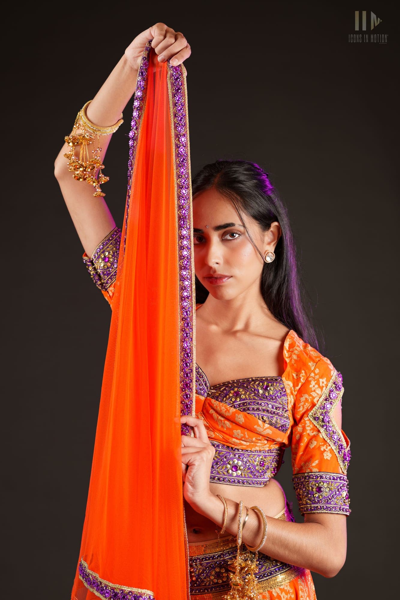 Dancer in orange and purple traditional dress holding a dupatta aloft