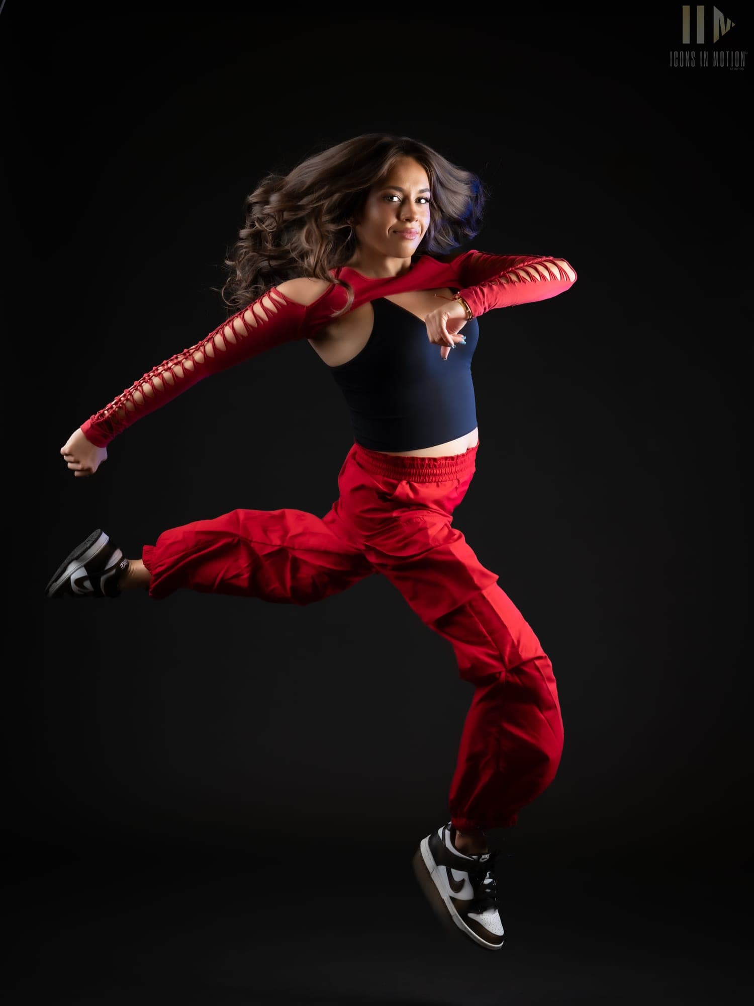 Dancer in red leaping mid-air with arms outstretched against a black backdrop