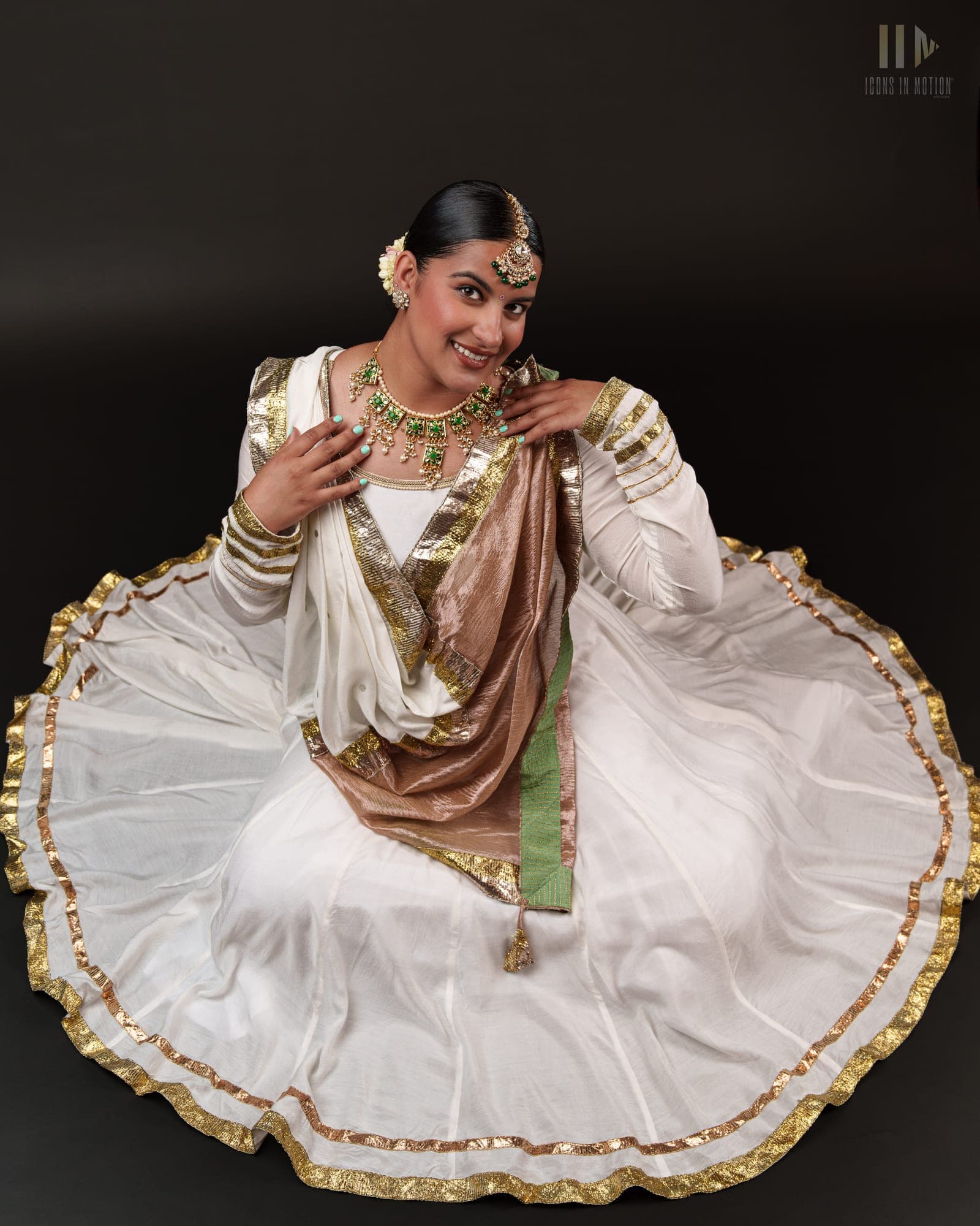 Classical dancer kneeling with a white and gold skirt fanned into a circle