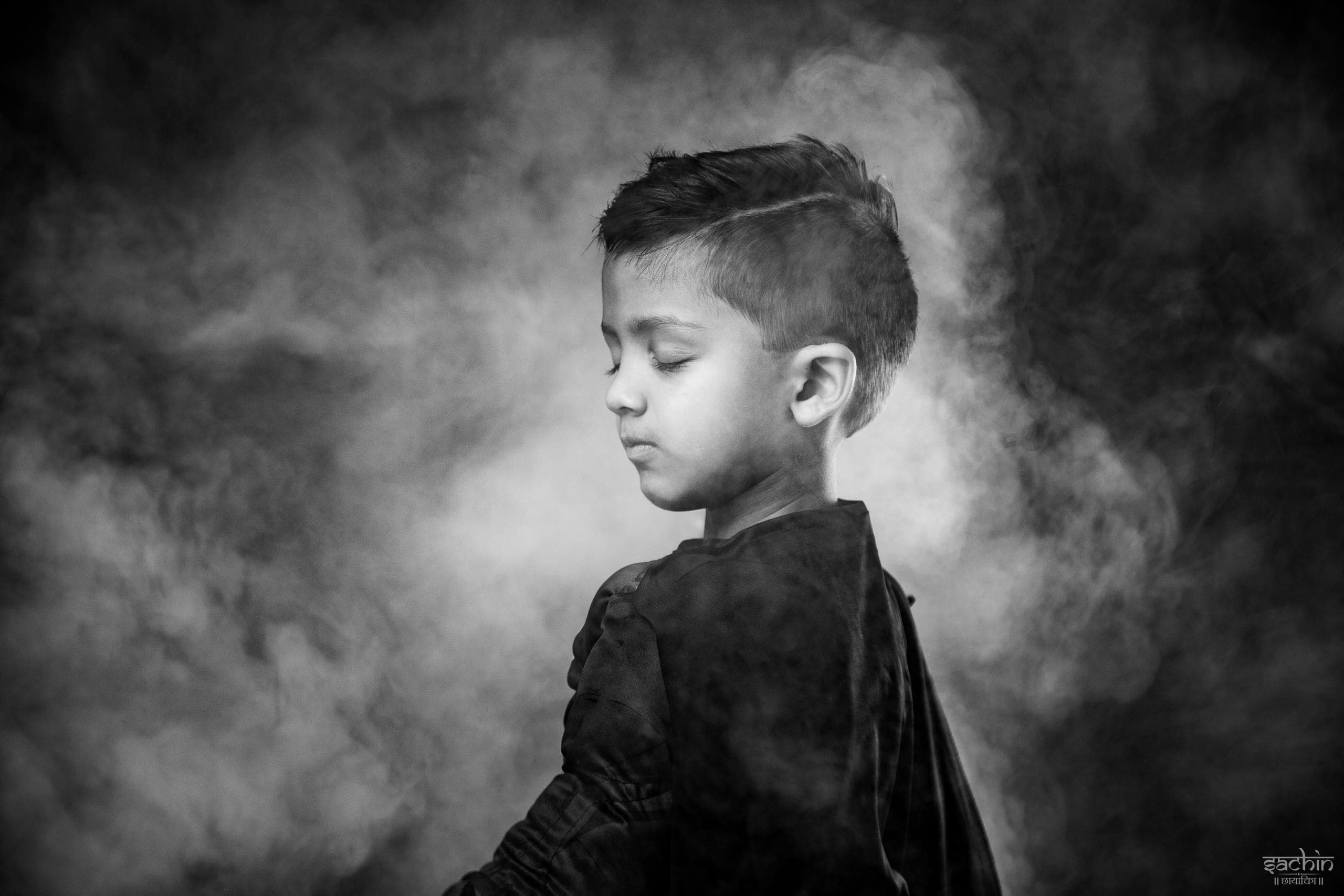Black and white portrait of a young boy with eyes closed against drifting smoke