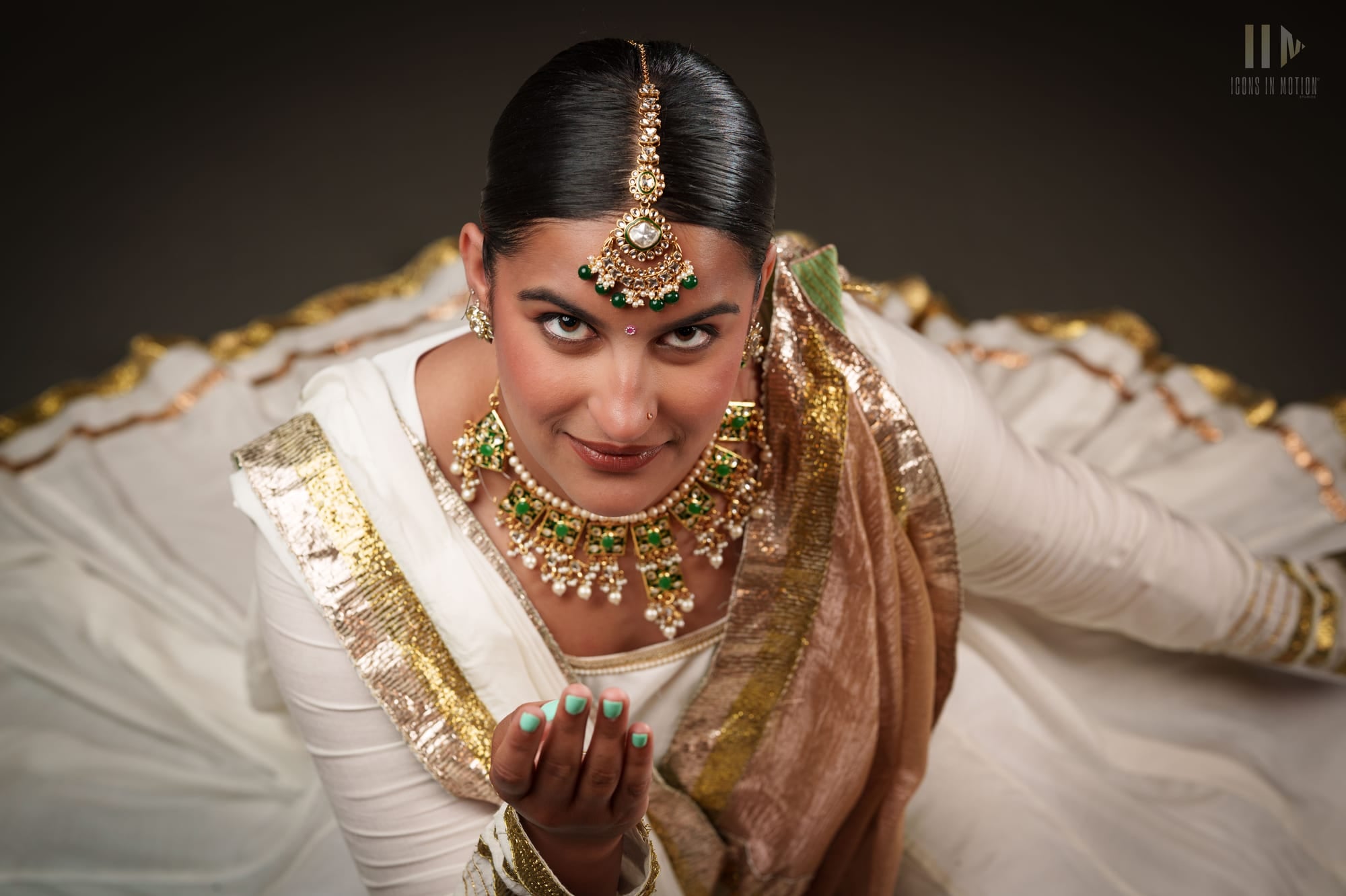 Classical dancer seated in white and gold, hands held in a mudra, looking at the camera